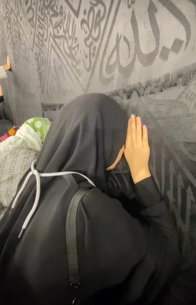 Mujer musulmana apoyada en la pared de la Kaaba.